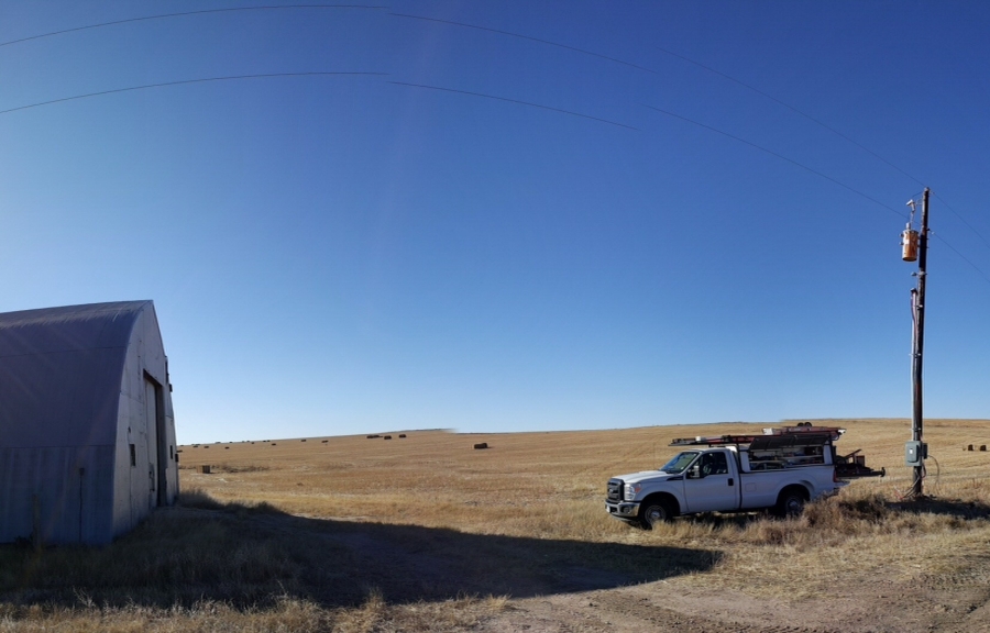 Agricultural electrician service truck beside a rural power pole and farm building in Colorado.